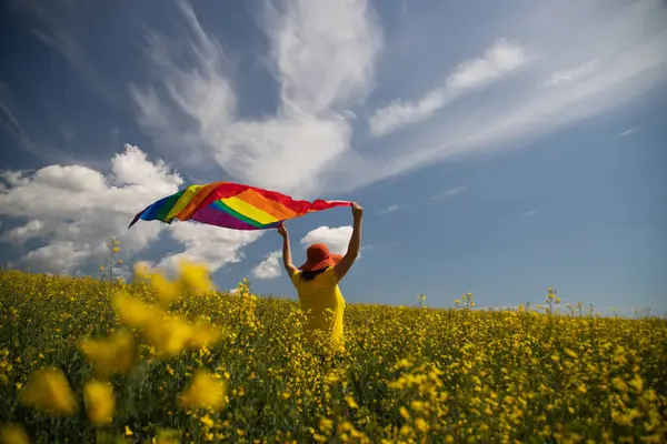 Çayırda LGTB bayrağı sallayan ikili olmayan kişi. LGBT gurur kavramı.