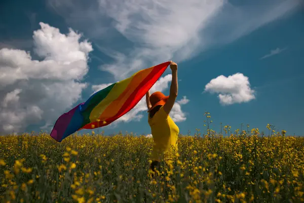 Çayırda LGTB bayrağı sallayan ikili olmayan kişi. LGBT gurur kavramı.