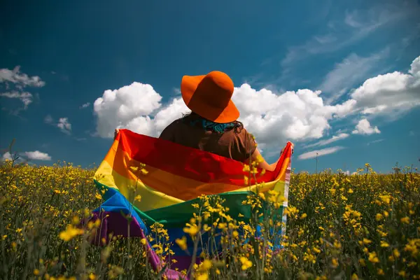 Çayırda LGTB bayrağı sallayan ikili olmayan kişi. LGBT gurur kavramı.