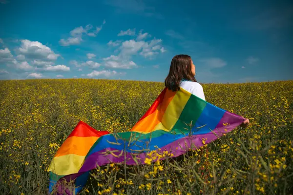 Çayırda LGTB bayrağı sallayan ikili olmayan kişi. LGBT gurur kavramı.