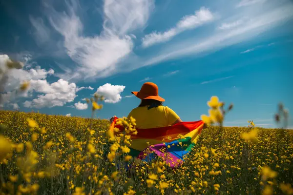 Çayırda LGTB bayrağı sallayan ikili olmayan kişi. LGBT gurur kavramı.