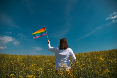 Çayırda LGTB bayrağı sallayan ikili olmayan kişi. LGBT gurur kavramı.