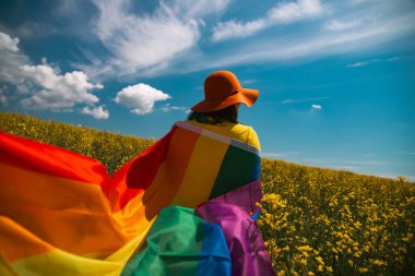 Çayırda LGTB bayrağı sallayan ikili olmayan kişi. LGBT gurur kavramı.