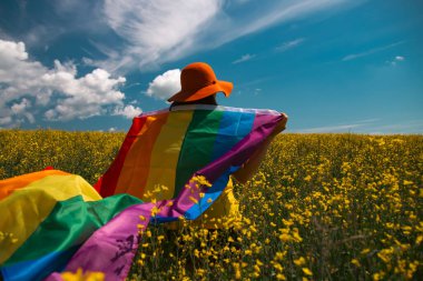 Çayırda LGTB bayrağı sallayan ikili olmayan kişi. LGBT gurur kavramı.