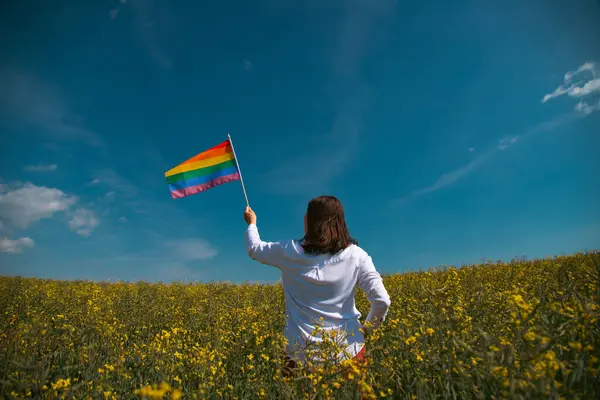 Çayırda LGTB bayrağı sallayan ikili olmayan kişi. LGBT gurur kavramı.