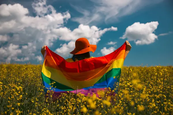 Çayırda LGTB bayrağı sallayan ikili olmayan kişi. LGBT gurur kavramı.