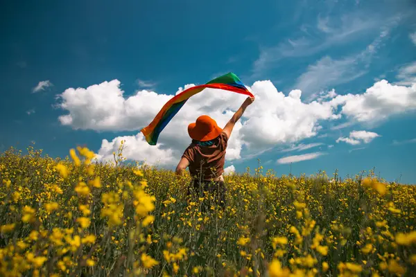 Çayırda LGTB bayrağı sallayan ikili olmayan kişi. LGBT gurur kavramı.