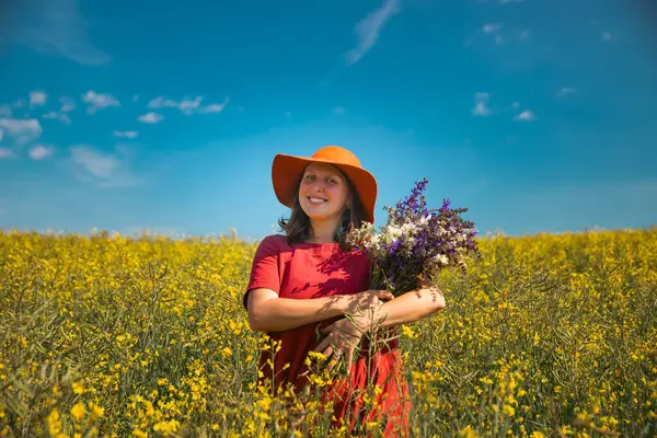 Güzel bir kadın elinde bir buket yaban çiçeği tutuyor, muhteşem doğanın tadını çıkarıyor. Yaz yaşam tarzı konsepti.