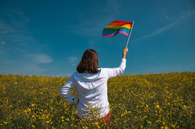 Çayırda LGTB bayrağı sallayan ikili olmayan kişi. LGBT gurur kavramı.