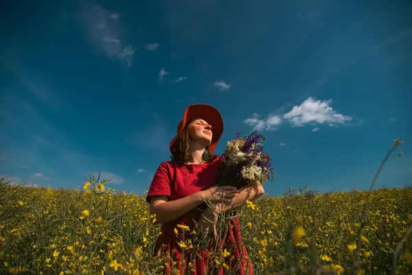 Güzel bir kadın elinde bir buket yaban çiçeği tutuyor, muhteşem doğanın tadını çıkarıyor. Yaz yaşam tarzı konsepti.