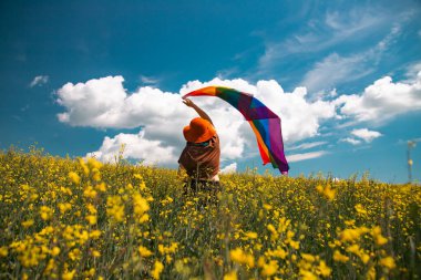 Çayırda LGTB bayrağı sallayan ikili olmayan kişi. LGBT gurur kavramı.