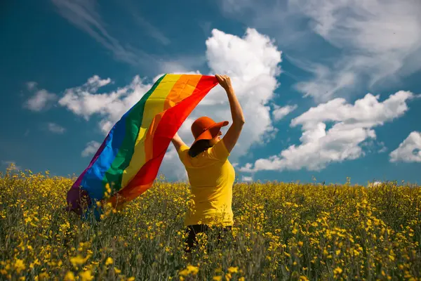 Çayırda LGTB bayrağı sallayan ikili olmayan kişi. LGBT gurur kavramı.