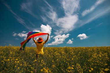 Çayırda LGTB bayrağı sallayan ikili olmayan kişi. LGBT gurur kavramı.