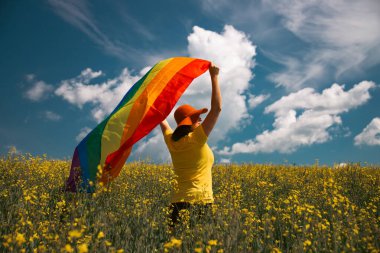 Çayırda LGTB bayrağı sallayan ikili olmayan kişi. LGBT gurur kavramı.