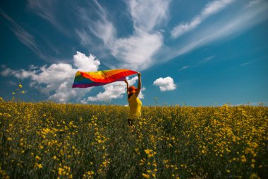 Çayırda LGTB bayrağı sallayan ikili olmayan kişi. LGBT gurur kavramı.