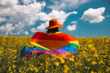 Çayırda LGTB bayrağı sallayan ikili olmayan kişi. LGBT gurur kavramı.