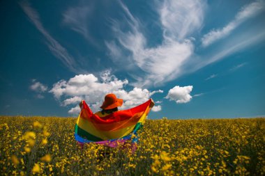 Çayırda LGTB bayrağı sallayan ikili olmayan kişi. LGBT gurur kavramı.