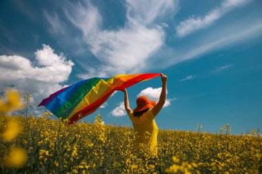 Çayırda LGTB bayrağı sallayan ikili olmayan kişi. LGBT gurur kavramı.