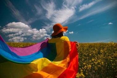 Çayırda LGTB bayrağı sallayan ikili olmayan kişi. LGBT gurur kavramı.