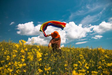 Çayırda LGTB bayrağı sallayan ikili olmayan kişi. LGBT gurur kavramı.