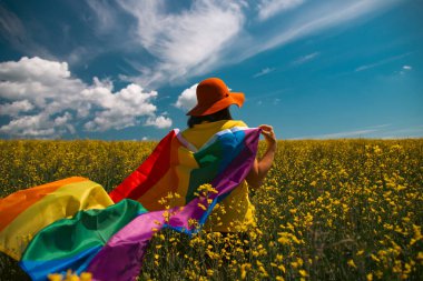 Çayırda LGTB bayrağı sallayan ikili olmayan kişi. LGBT gurur kavramı.