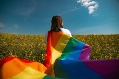 Çayırda LGTB bayrağı sallayan ikili olmayan kişi. LGBT gurur kavramı.