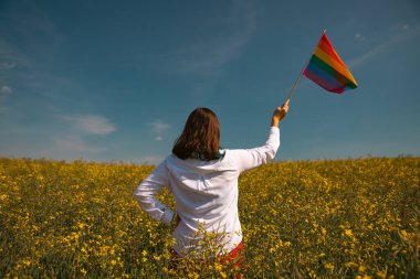 Çayırda LGTB bayrağı sallayan ikili olmayan kişi. LGBT gurur kavramı.