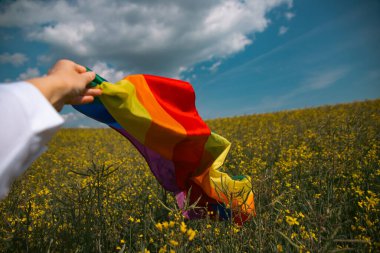Çayırda LGTB bayrağı sallayan ikili olmayan kişi. LGBT gurur kavramı.