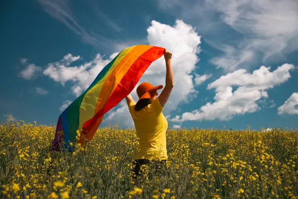 Çayırda LGTB bayrağı sallayan ikili olmayan kişi. LGBT gurur kavramı.