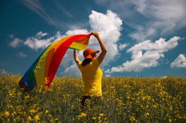 Çayırda LGTB bayrağı sallayan ikili olmayan kişi. LGBT gurur kavramı.