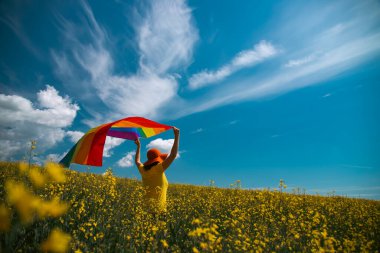 Çayırda LGTB bayrağı sallayan ikili olmayan kişi. LGBT gurur kavramı.