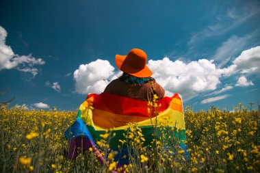 Çayırda LGTB bayrağı sallayan ikili olmayan kişi. LGBT gurur kavramı.