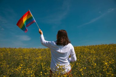 Çayırda LGTB bayrağı sallayan ikili olmayan kişi. LGBT gurur kavramı.