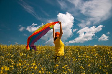 Çayırda LGTB bayrağı sallayan ikili olmayan kişi. LGBT gurur kavramı.