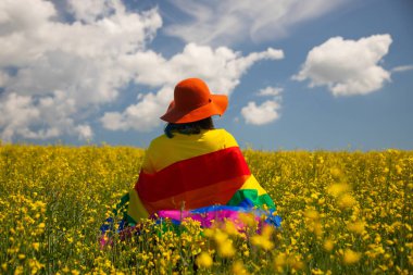 Çayırda LGTB bayrağı sallayan ikili olmayan kişi. LGBT gurur kavramı.