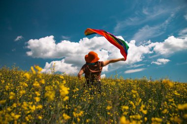 Çayırda LGTB bayrağı sallayan ikili olmayan kişi. LGBT gurur kavramı.