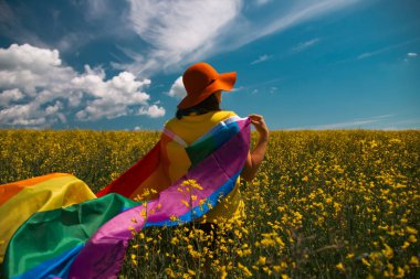 Çayırda LGTB bayrağı sallayan ikili olmayan kişi. LGBT gurur kavramı.