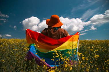 Çayırda LGTB bayrağı sallayan ikili olmayan kişi. LGBT gurur kavramı.