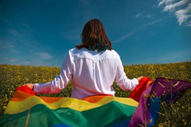 Çayırda LGTB bayrağı sallayan ikili olmayan kişi. LGBT gurur kavramı.