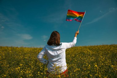 Çayırda LGTB bayrağı sallayan ikili olmayan kişi. LGBT gurur kavramı.