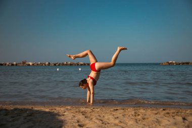 Mutlu kız sahilde amuda kalkıyor. Seyahat, yaz, tatil, enerji kavramı.