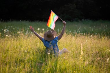 Çayırda LGTB bayrağı sallayan ikili olmayan kişi. LGBT gurur kavramı.