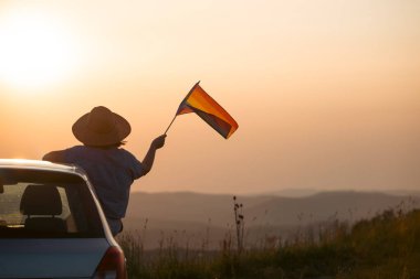 Gün batımında arabada LGTB bayrağı sallayan ikili olmayan kişi. LGBT gurur kavramı.