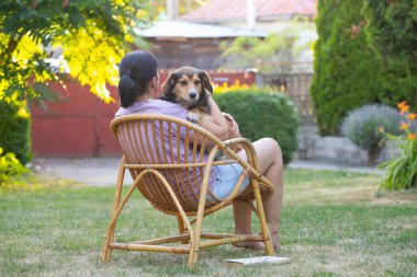 Sıradan, orta yaşlı bir kadın bahçede küçük kahverengi köpeğiyle eğleniyor. Hayvanlarla bağ kurma ve birlikte olmaktan keyif alma kavramı.