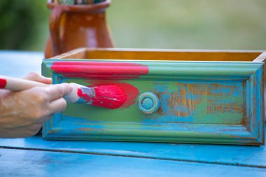 İnsan eli tebeşirle ahşap mobilya boyuyor. Yepyeni renkli tebeşir boyasıyla eski moda ahşap mobilyaları yeniliyorum. Ev dekorasyonu yeniden biçimlendiriliyor