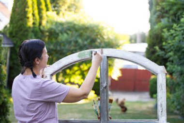 Orta yaşlı bir kadın ahşap mobilya boyuyor. Yepyeni renkli tebeşir boyasıyla eski moda ahşap mobilyaları yeniliyorum. Ev dekorasyonu yeniden biçimlendiriliyor