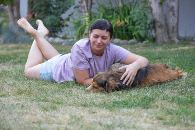 Sıradan, orta yaşlı bir kadın bahçede küçük kahverengi köpeğiyle eğleniyor. Hayvanlarla bağ kurma ve birlikte olmaktan keyif alma kavramı.