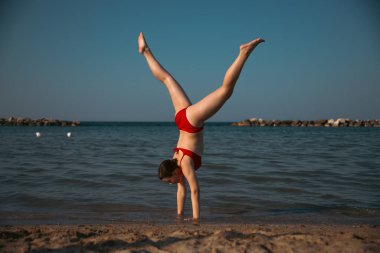 Mutlu kız sahilde amuda kalkıyor. Seyahat, yaz, tatil, enerji kavramı.