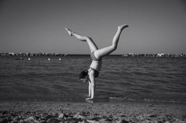 Mutlu kız sahilde amuda kalkıyor. Seyahat, yaz, tatil, enerji kavramı.