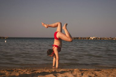 Mutlu kız sahilde amuda kalkıyor. Seyahat, yaz, tatil, enerji kavramı.